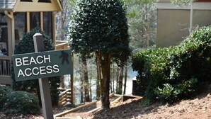 A sign indicating beach access, surrounded by a wooden deck, a small tree, and a building in the background. - Lake-Front Family Home in Big Canoe (Jasper)