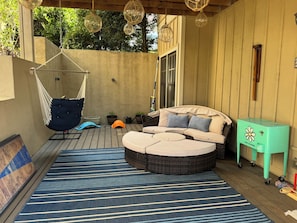 Un patio al aire libre cubierto con una silla colgante, un sofá redondo de mimbre y una pequeña mesa.