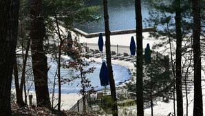 A lakeside area with a wooden deck, benches, and umbrellas. - Lake-Front Family Home in Big Canoe (Jasper)