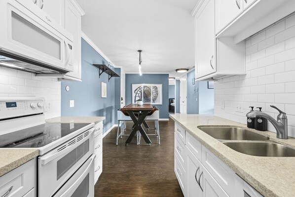 A modern kitchen with white cabinetry, a wooden dining table, and a stainless steel sink. - Ocean View La Jolla Condo - Steps to Beach (San Diego)