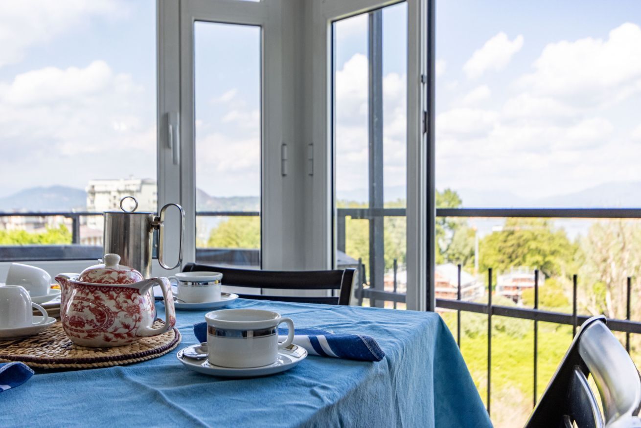 Een balkon met een theetafel, uitzicht op zee en een gebouw op de achtergrond.