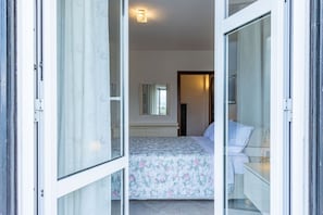 Eine offene Schiebetür führt in ein Schlafzimmer mit einem Bett, einem Nachttisch und einem Spiegel.