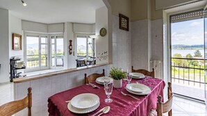 Un coin repas avec une table dressée pour quatre personnes, une plante en pot et une vue sur l’extérieur.