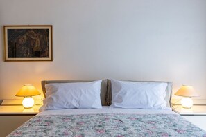 Een bed met een bloemenprint sprei, twee bedlampen en een lijst met kunstwerk aan de muur.