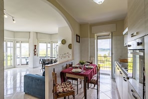 Een ruime eetruimte met een tafel voor vier personen, een blauwe bank en een keuken met roestvrijstalen apparatuur.