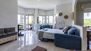 Une pièce spacieuse comprenant un lit, un canapé, un bureau et une chaise. Elle est dotée de grandes fenêtres et d’un balcon.
