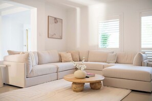 Una sala de estar moderna con un sofá seccional color beige, una mesa de centro redonda de madera y un tapete blanco.