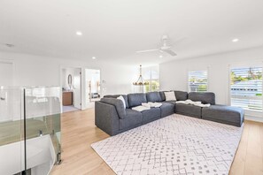A modern living room with a sectional sofa, a glass railing, and a patterned rug. - Whitesands by Aryve | Robina (Robina)