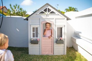 A small, single-story playhouse with a pink door and windows, number 45, situated on a grassy area. - Whitesands by Aryve | Robina (Robina)