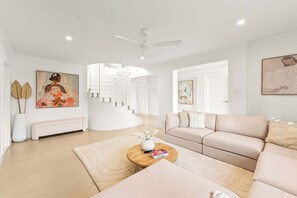 A modern living room with a curved staircase, a sofa set, and a coffee table with a book. - Whitesands by Aryve | Robina (Robina)