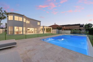 Una casa moderna de dos pisos con piscina, patio y césped bien cuidado.