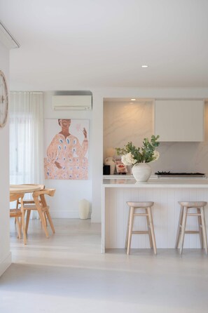 A modern kitchen with a central island, wooden stools, and a large abstract painting on the wall. - Whitesands by Aryve | Robina (Robina)