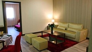 Une chambre d’hôtel avec un canapé, des poufs, une table, une lampe et une vue sur le couloir.