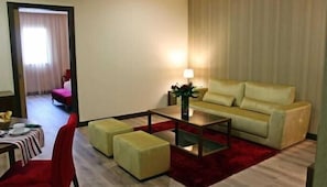 Ein Hotelzimmer mit Sofa, Hocker, Tisch, Lampe und Blick auf den Flur.