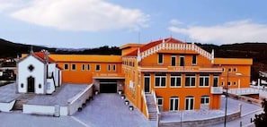 Ein Gebäude mit einem zentralen Eingang, einem kleineren Anbau und einer Treppe, die zum Haupteingang führt.