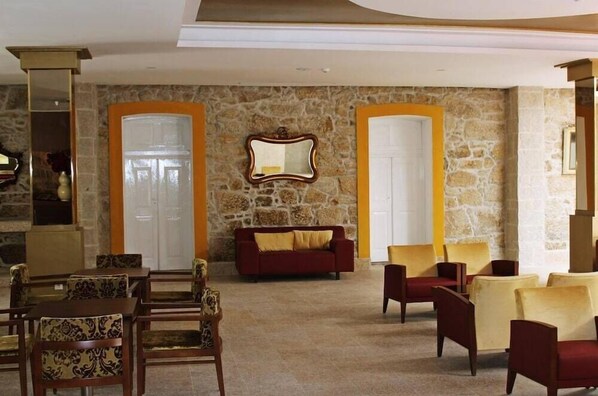 Una hall con pareti in pietra, un divano rosso e una sala da pranzo con sedie a fantasia.