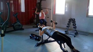Une salle de sport équipée de matériel d’exercice, avec un banc de développé et une personne qui soulève des poids.
