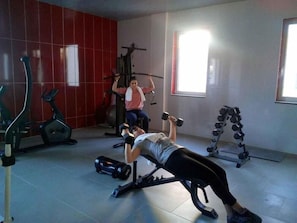 Ein Fitnessstudio mit Trainingsgeräten, einer Hantelbank und einer Person beim Gewichtheben.