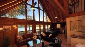 Interior espacioso de una cabaña con comedor, cocina y grandes ventanales con vistas a un lago.