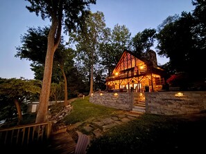 A large, two-story log cabin with a stone foundation, surrounded by trees and a stone pathway. - Main Channel Point Lot Lakefront Retreat - Sweeping Views, Private Dock + Lift (Lake Norman of Catawba)