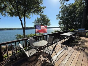 A deck with a table and chairs, overlooking a lake with an American flag. - Main Channel Point Lot Lakefront Retreat - Sweeping Views, Private Dock + Lift (Lake Norman of Catawba)