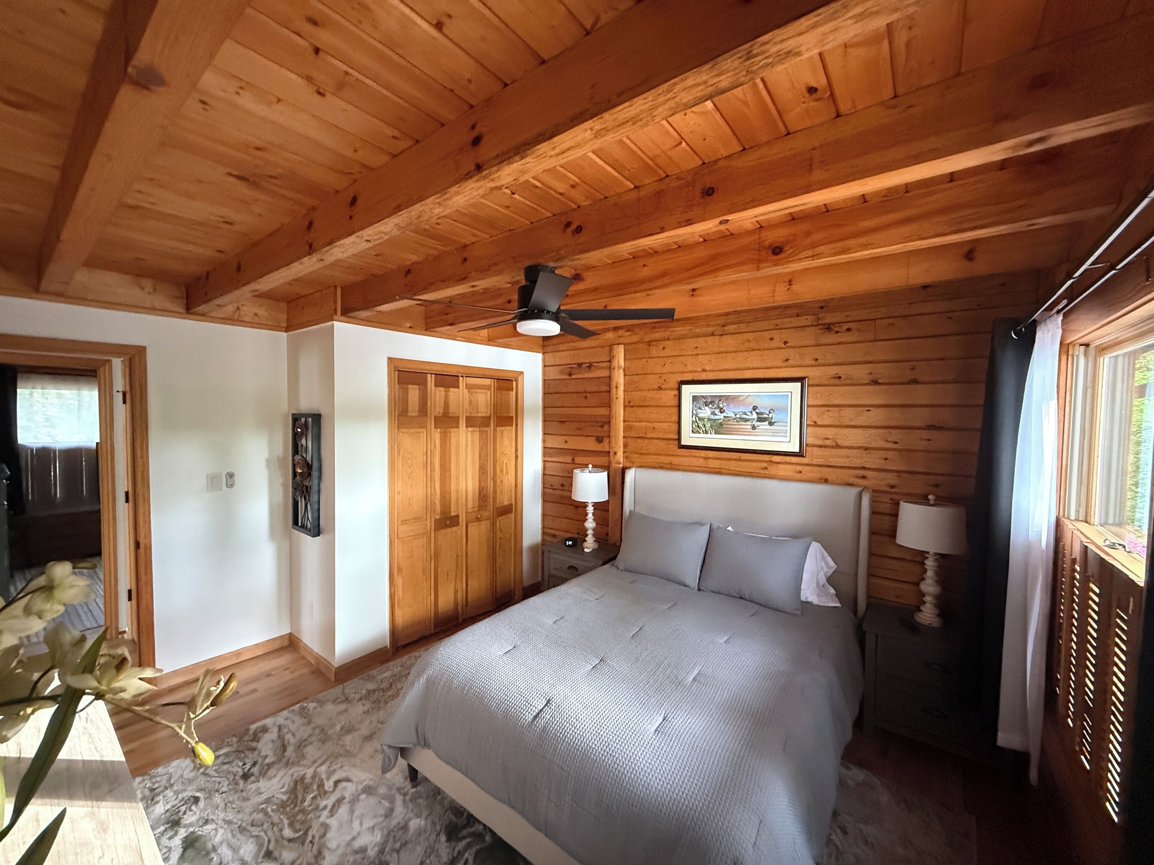 Un dormitorio con una cama, un ventilador de techo, un cuadro en la pared y paredes de madera.