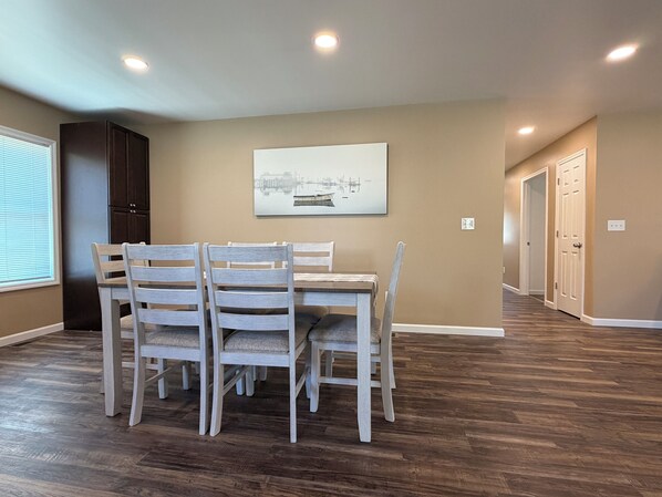 A dining area with a table and chairs, a painting on the wall, and a hallway with doors.