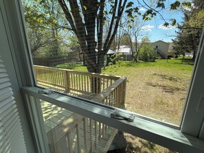 A view through a window of a wooden deck, a tree, and a grassy yard with a house in the background.