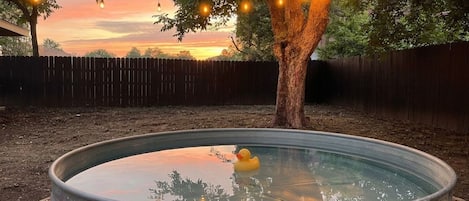 A metal barrel pool with a rubber duck, surrounded by a wooden fence, under a canopy with string lights.