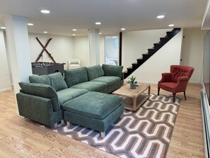 A living room with a sectional sofa, a red armchair, a wooden coffee table, and a patterned rug.