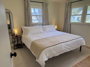 A bedroom with a bed, two bedside lamps, a window with curtains, and a door with a knob.