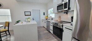 A modern kitchen with white cabinetry, a central island, a built-in oven, and a microwave.