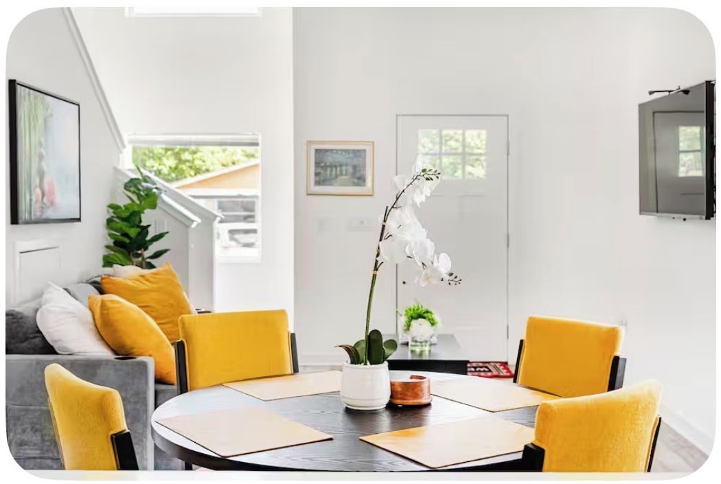 A dining area with a round table, yellow chairs, and a potted orchid.