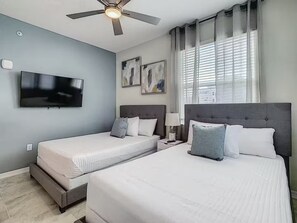 Ett hotellrum med två sängar, en takfläkt, en TV, konstverk på väggen och ett fönster med persienner.