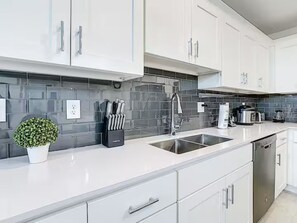 A modern kitchen with white cabinets, a stainless steel sink, and a tiled backsplash. - Modern Resort Condo Minutes to Disney (Kissimmee)