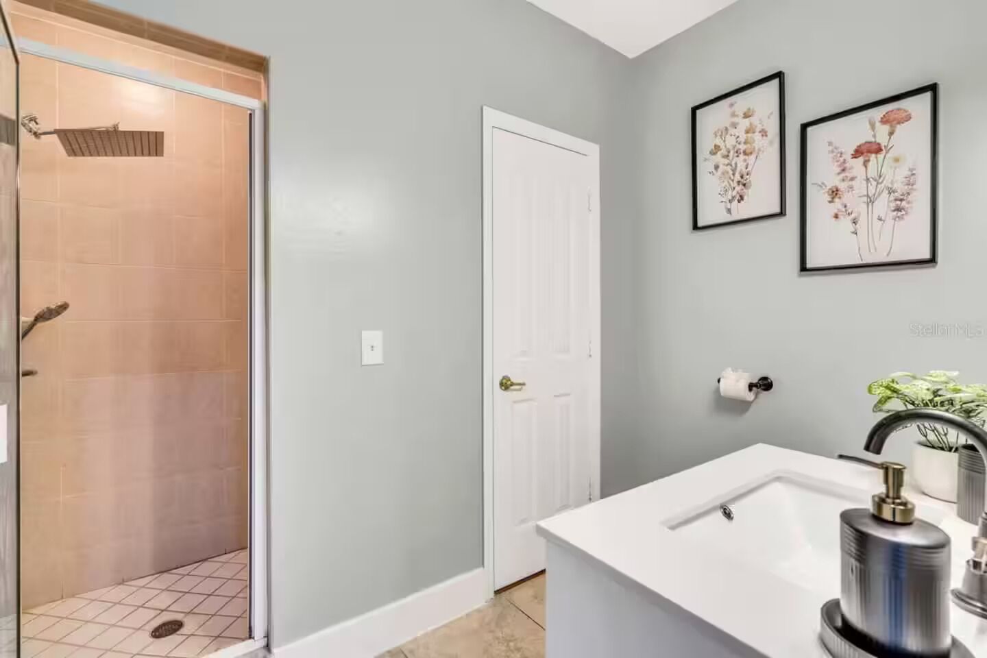 A bathroom with a shower, a sink, and two framed floral pictures on the wall.