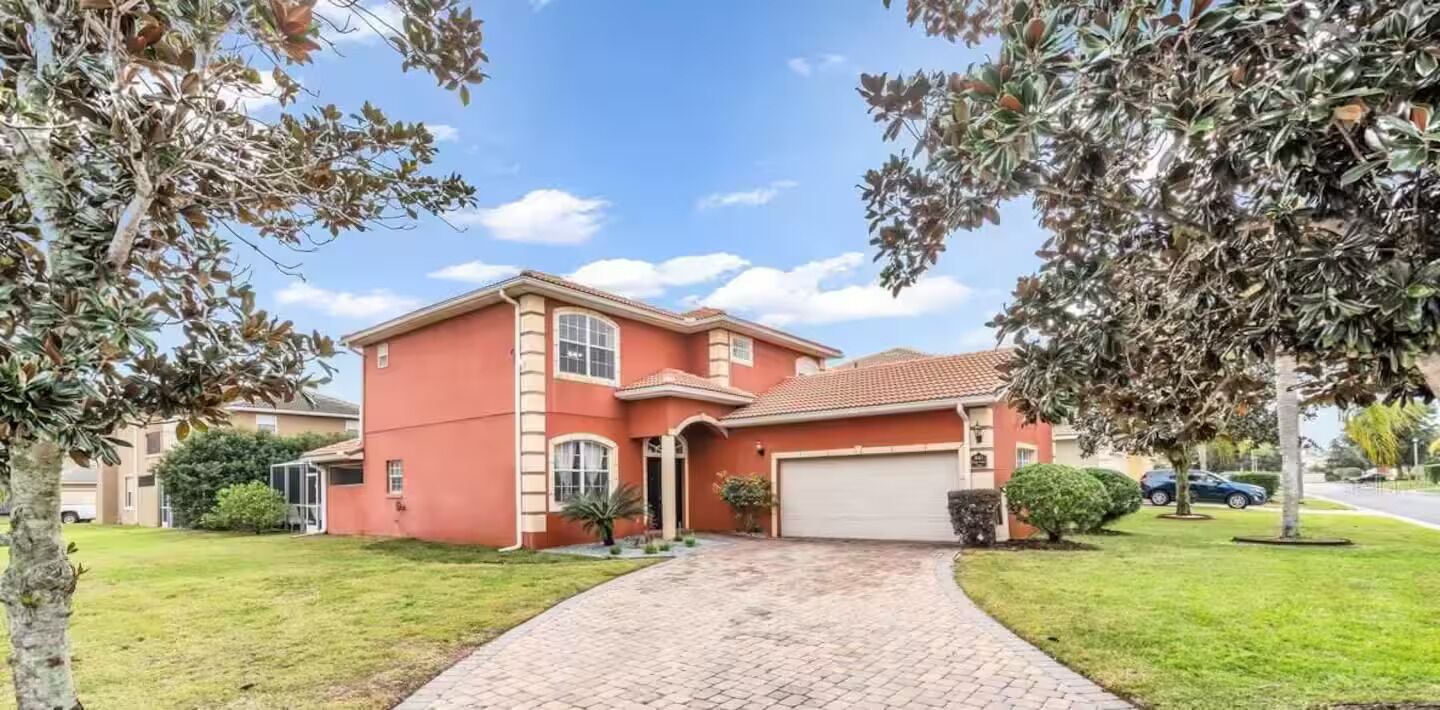 Une maison à deux étages avec une façade rouge, un garage et une allée pavée.