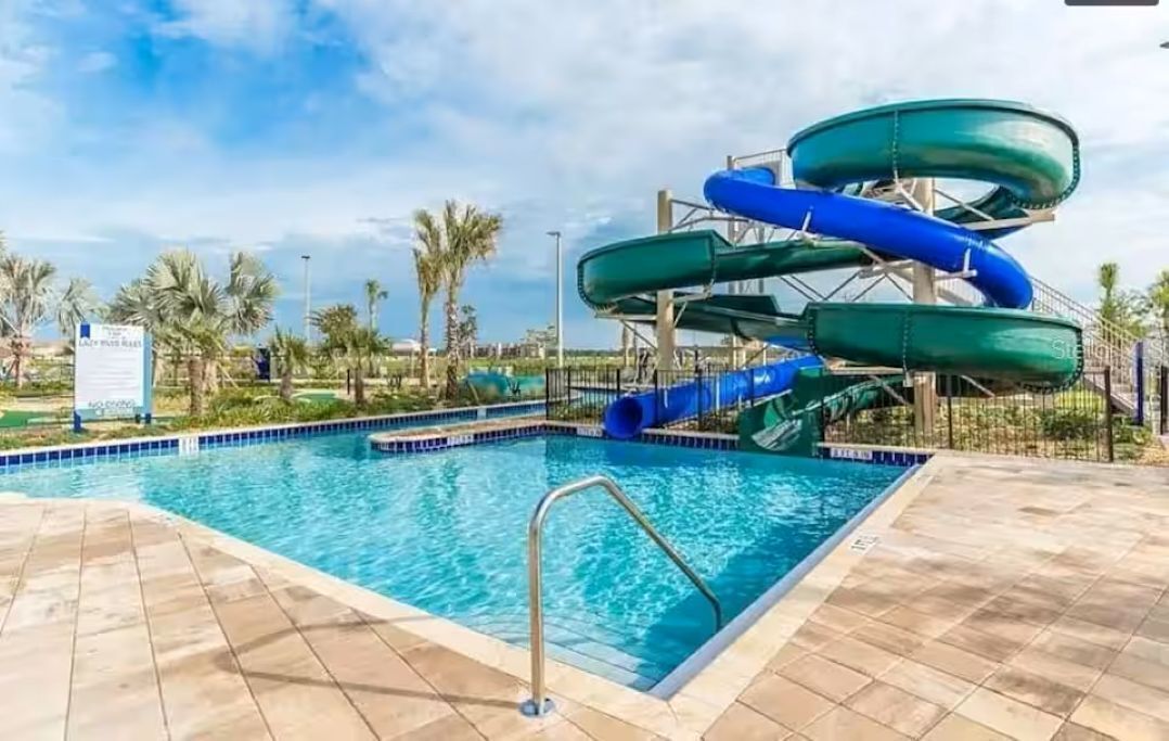 Une piscine avec un toboggan aquatique, des palmiers et un ciel dégagé.