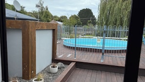 Eine Holzterrasse mit Schwimmbecken, umgeben von einem Metallzaun und Kübelpflanzen.