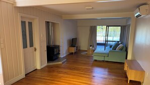 Ein geräumiges Wohnzimmer mit Holzboden, eingebautem Kamin, einer Couch, einem Fernseher und einer Glastür zum Garten.