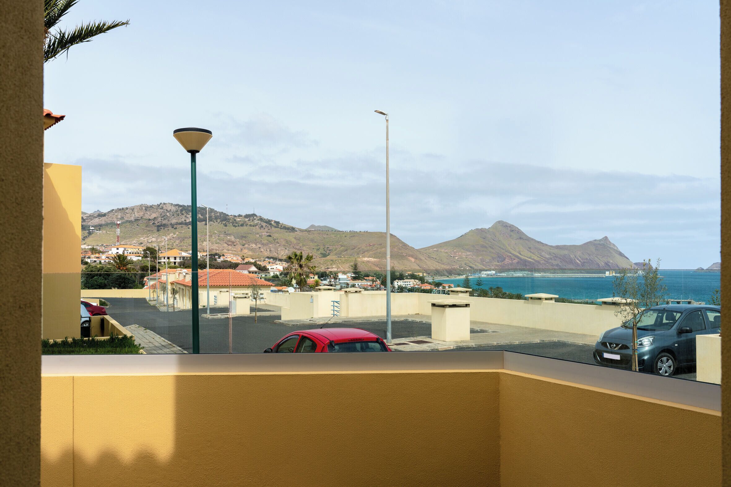 Vista da un balcone su un'area di parcheggio con auto, una montagna e un corpo d'acqua.