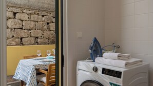 Un espace dédié à la lessive, avec un lave-linge, une table recouverte d’une nappe et un mur en pierre.
