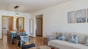 Un salon comprenant un canapé, une table à manger avec des chaises, une table basse avec un récipient, et un mur orné de tableaux encadrés.