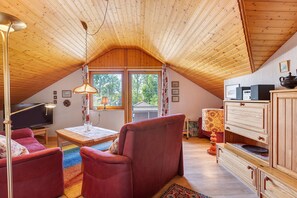 Ein gemütliches Dachzimmer mit Holzbalkendecke, einem roten Sofa, einem Esstisch und einem Fernseher.