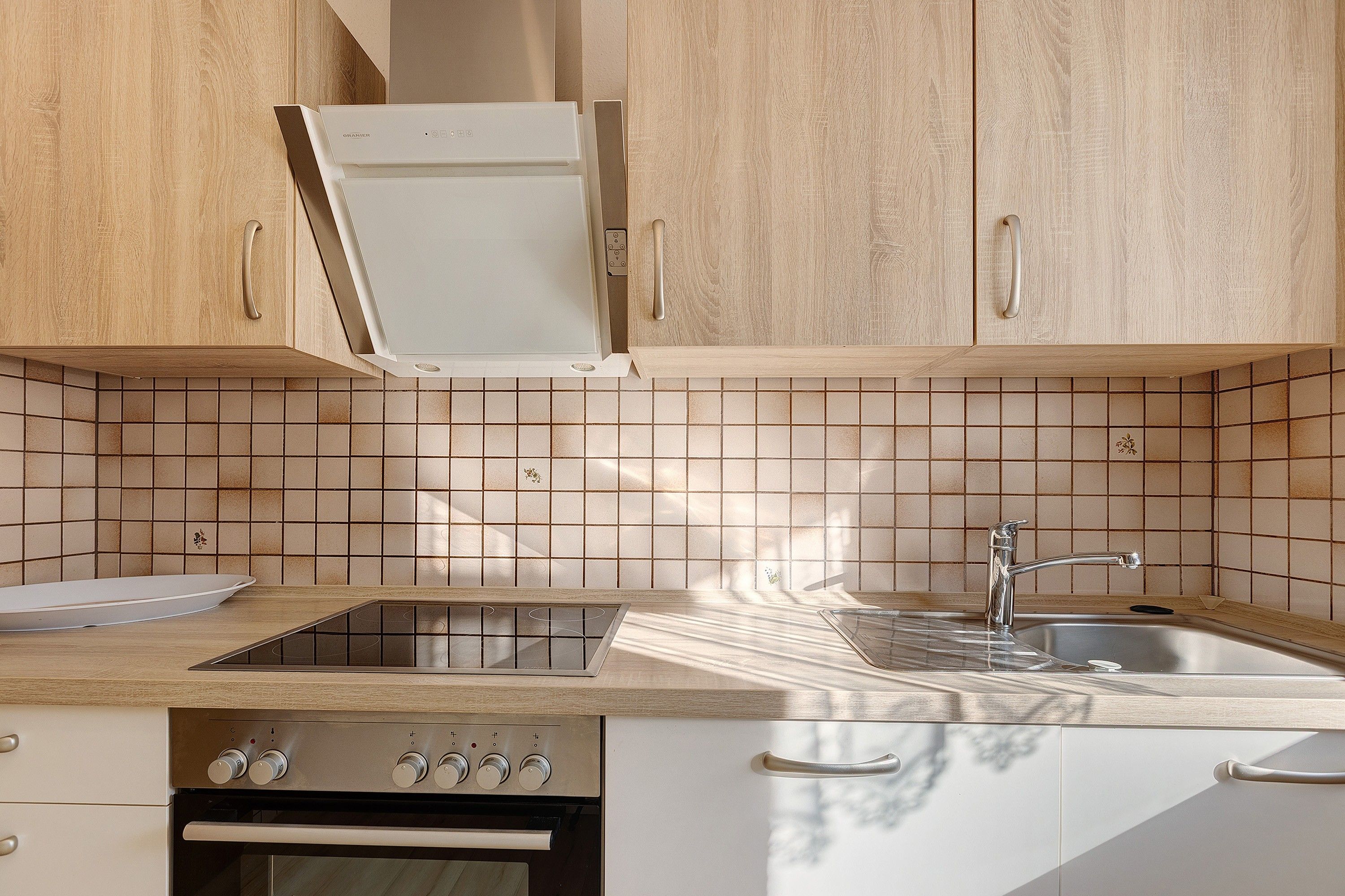 Eine Küche mit Holzschränken, einer Fliesenrückwand, einer Edelstahlspüle und einem eingebauten Backofen.