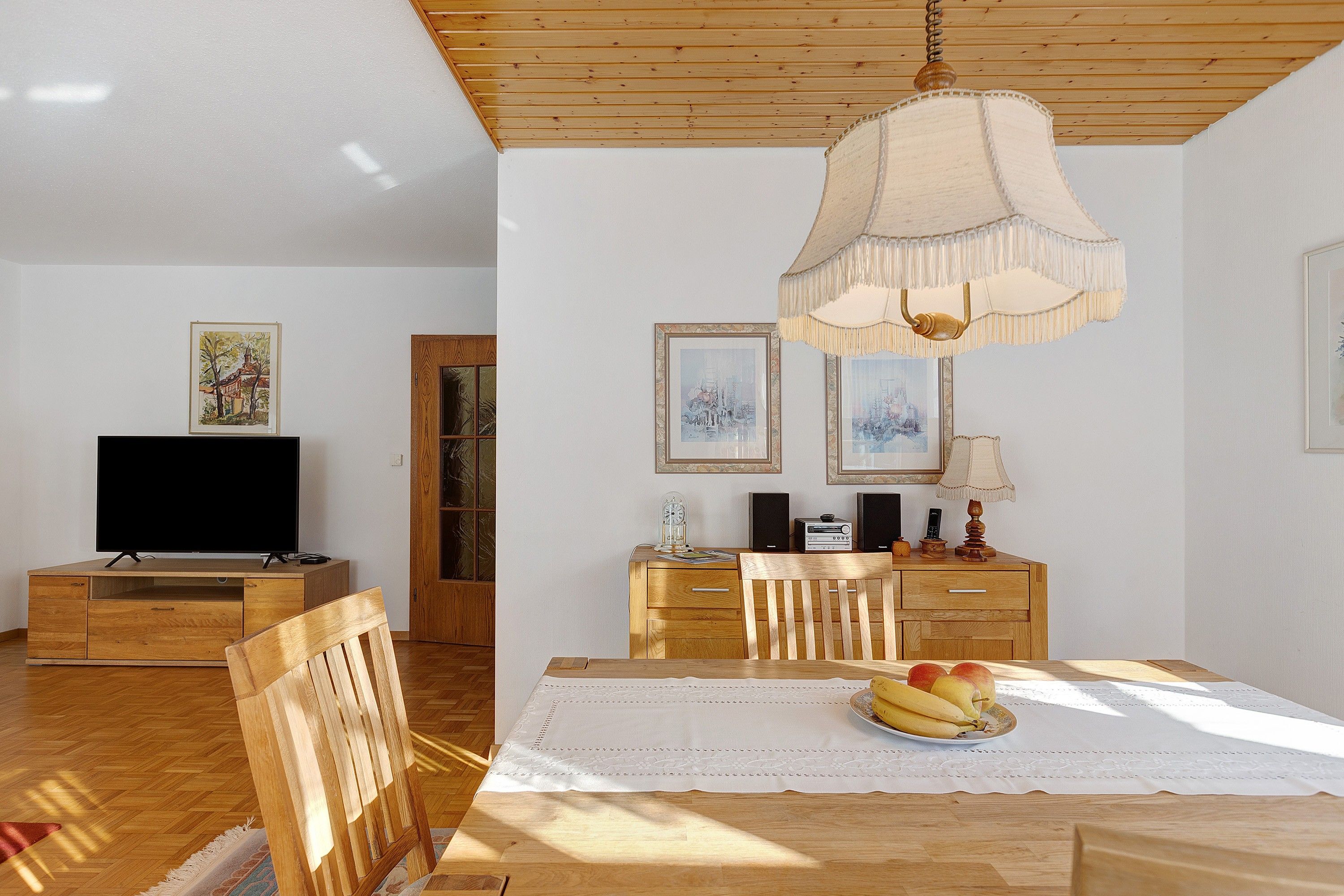 Un espace repas comprenant une table en bois, des chaises, un téléviseur et des œuvres d’art accrochées aux murs.