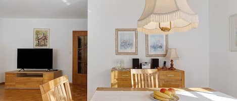 A dining area with a wooden table, chairs, a television, and artwork on the walls.