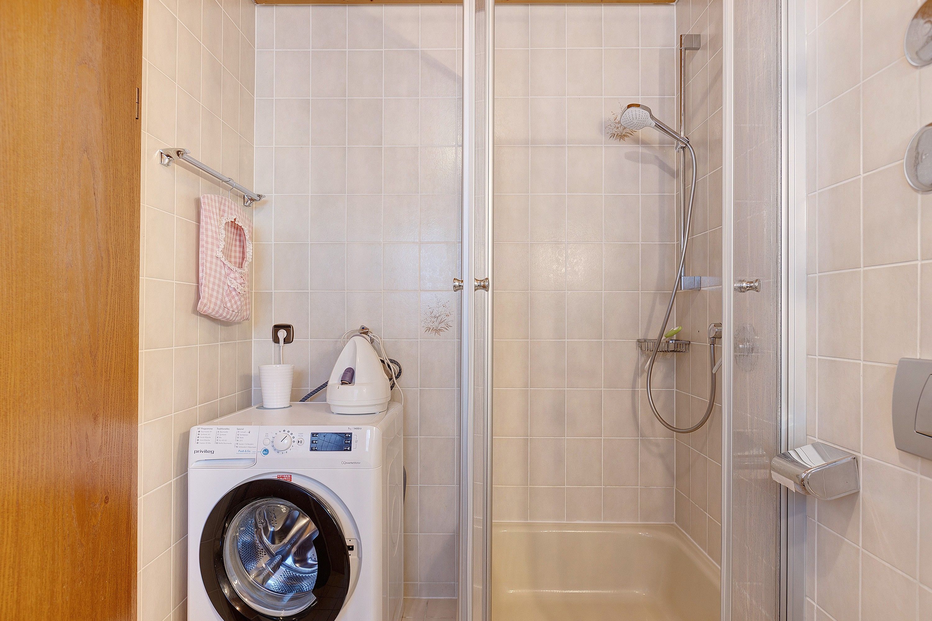 Ein kleines Badezimmer mit Waschmaschine, Dusche und Toilette.