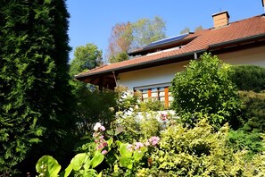 Ein Haus mit einem geneigten Dach, Solaranlagen und einem Garten mit verschiedenen Pflanzen und Blumen.