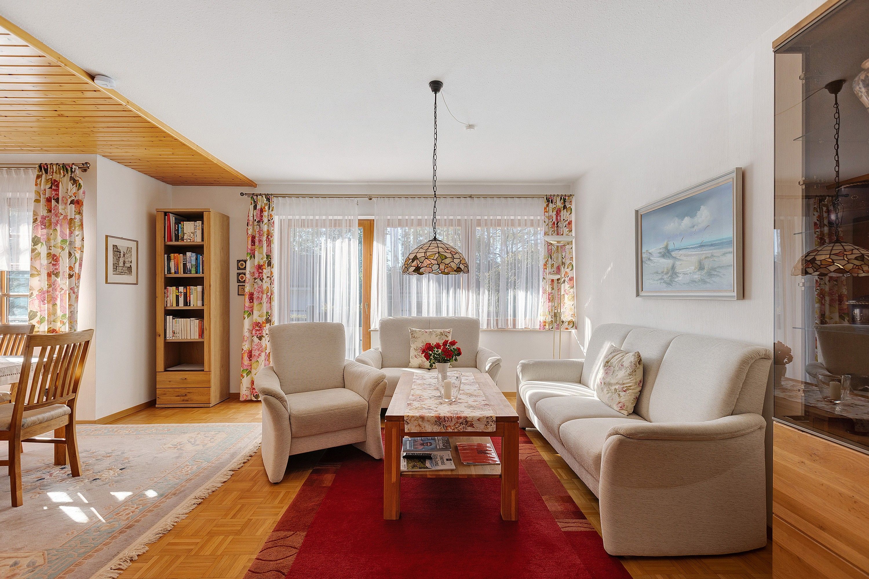 A living room with a wooden ceiling, a sofa set, a coffee table, a bookshelf, and a painting on the wall.